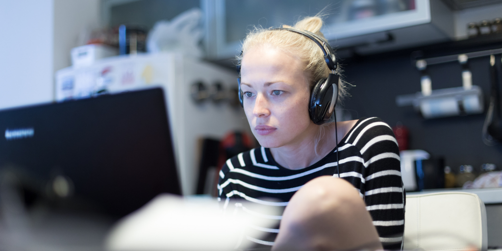 woman with headphones working at laptop in her kitchen