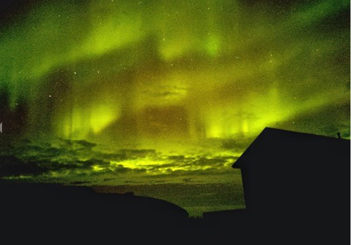 The aurora borealis, or northern lights, fill the night sky above a silhouette of a house.. The aurora borealis, or northern lights, fill the night sky above a silhouette of a house..
