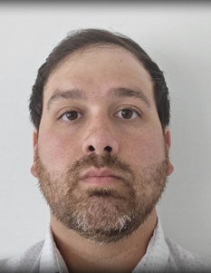 Professional headshot of a middle-aged man with dark hair and graying beard wearing a light gray collared shirt against a white background